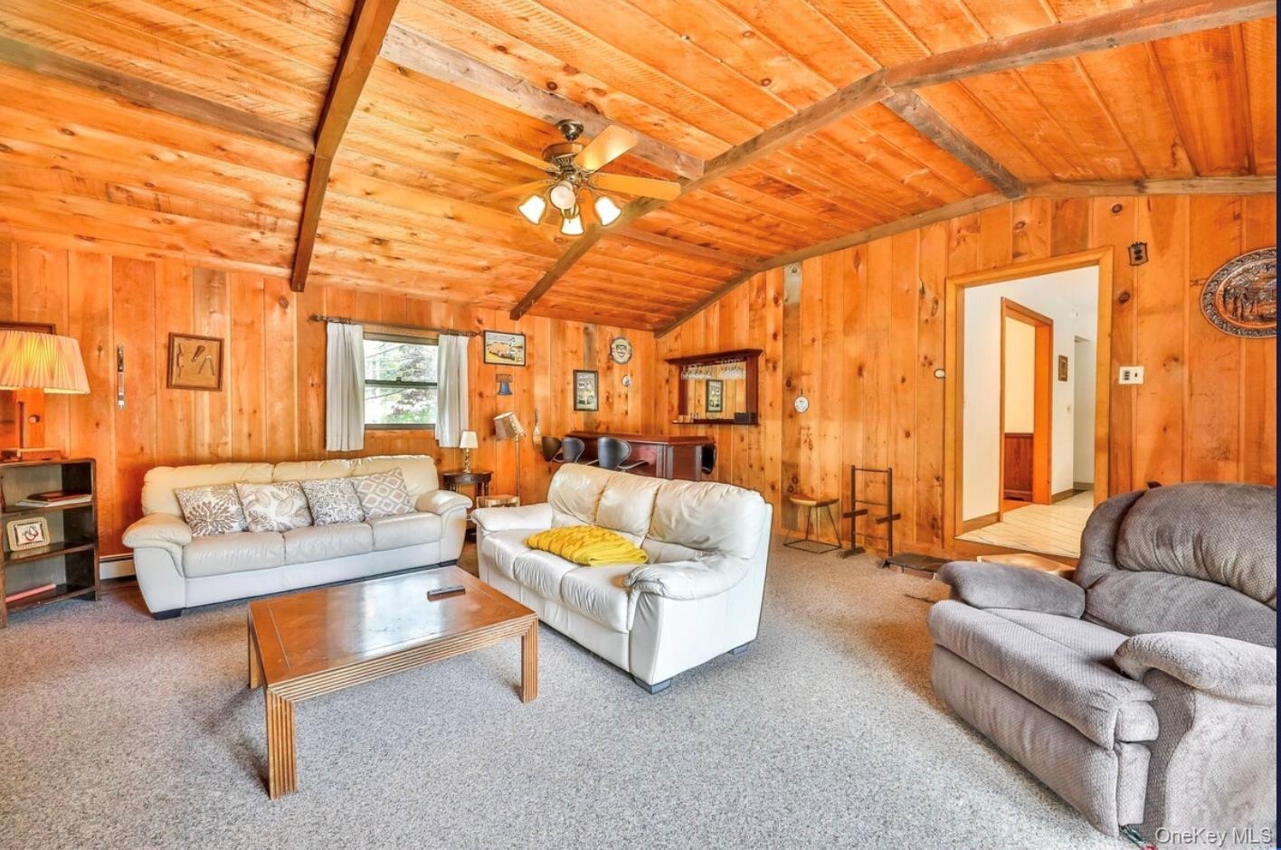 Carpeted living room with wooden walls, wood ceiling, and a ceiling fan