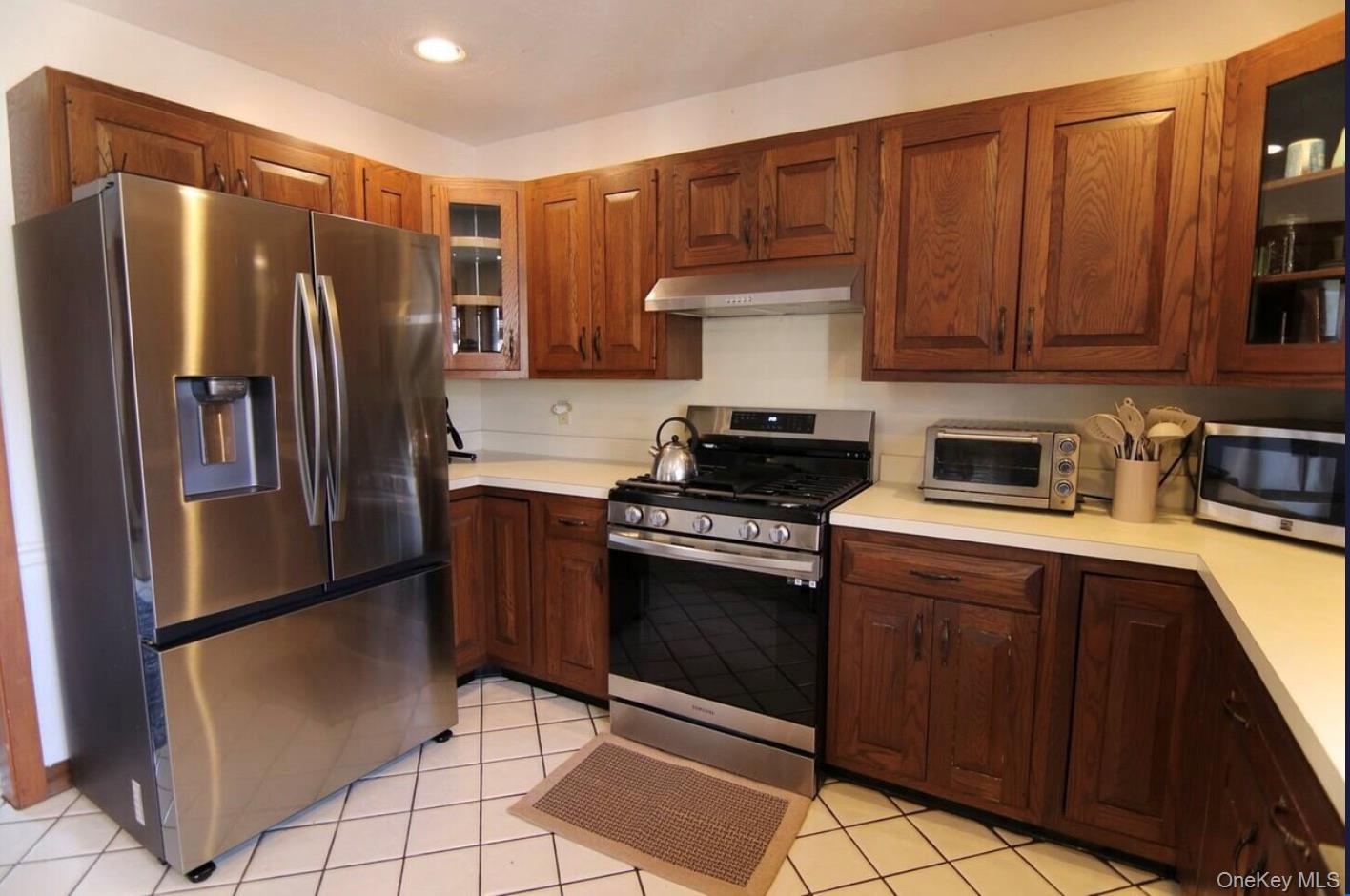 Kitchen featuring glass insert cabinets, appliances with stainless steel finishes, light countertops, light tile patterned floors, and recessed lighti