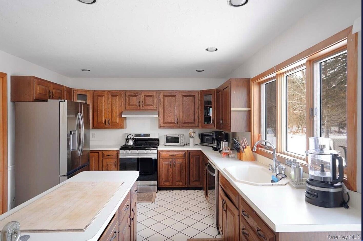 Kitchen featuring stainless steel appliances, brown cabinetry, light countertops, light tile patterned floors, and recessed lighting