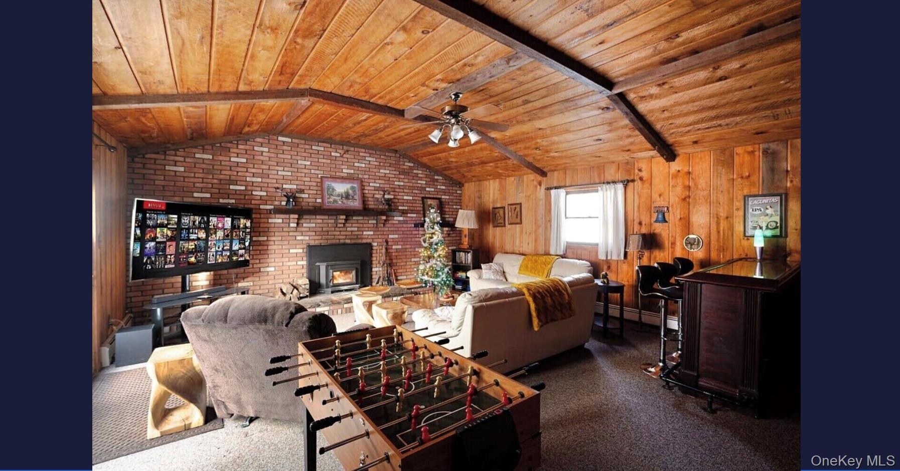 Living area featuring wood ceiling, a ceiling fan, brick wall, wooden walls, and a fireplace