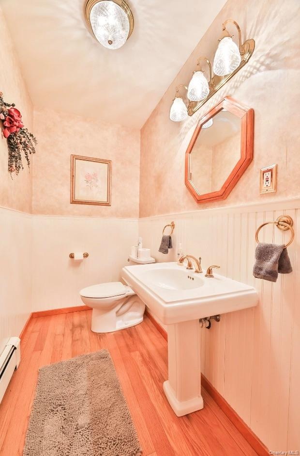 Half bath featuring a wainscoted wall, light wood-type flooring, and a baseboard heating unit