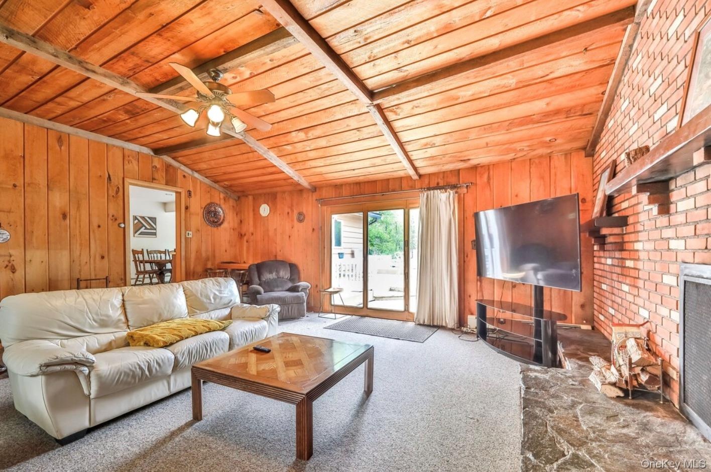 Carpeted living room with wood ceiling, ceiling fan, wooden walls, and a fireplace