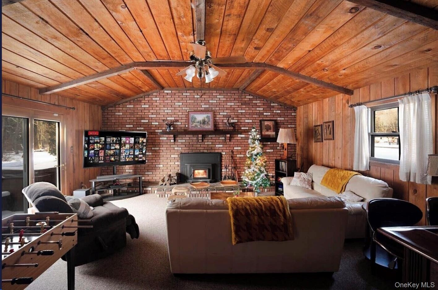Living area featuring wooden walls, wood ceiling, a ceiling fan, carpet flooring, and a wood stove