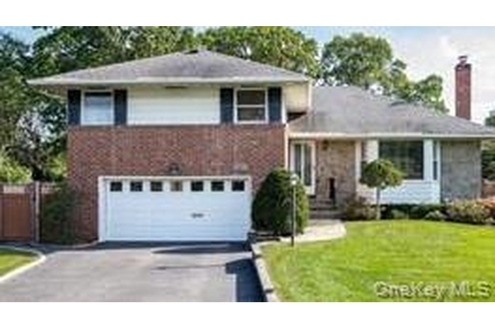 Split level home with driveway, an attached garage, a front lawn, and a chimney