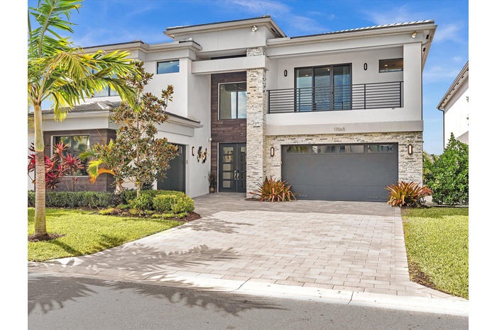 Modern elevation with clean architectural lines, lush landscaping, and an oversized paver driveway creating striking curb appeal.