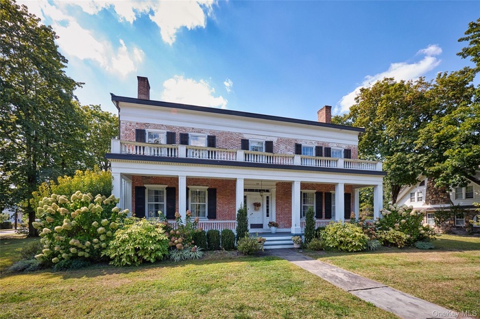 View of front of home with a chimney, brick siding, a front yard, and a porch