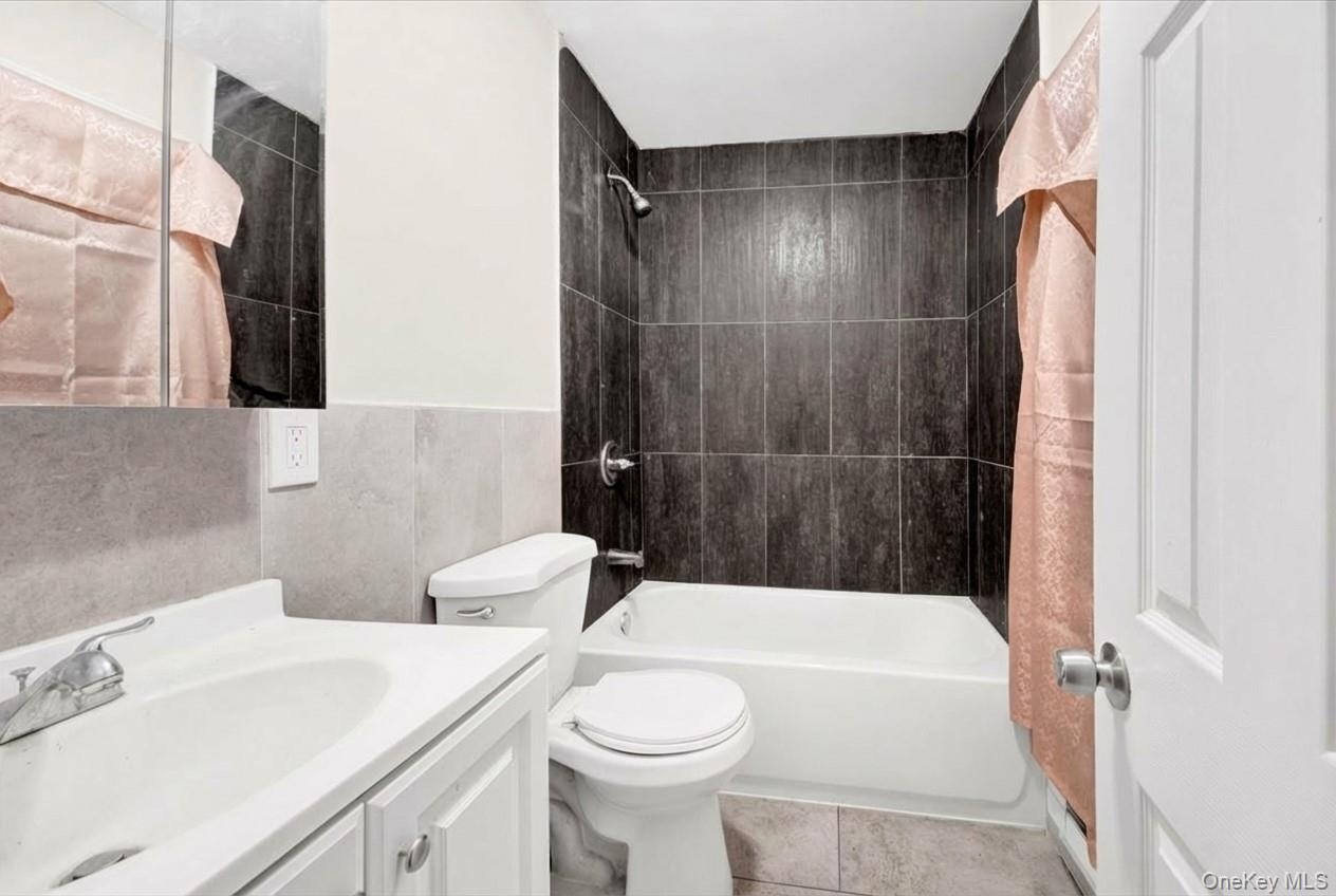 Bathroom featuring vanity, shower / bath combination with curtain, tile walls, a wainscoted wall, and light tile patterned floors