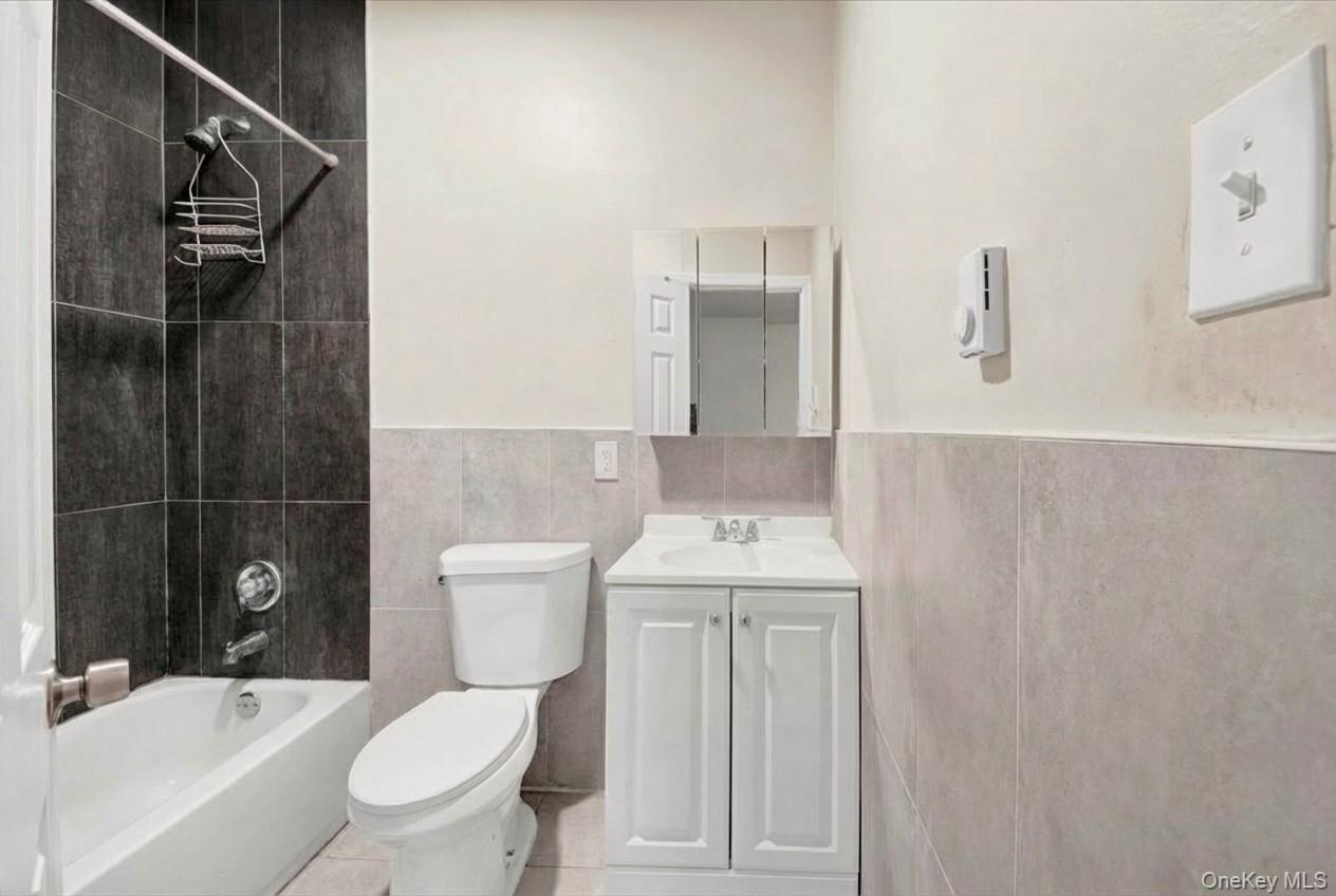 Full bath with vanity, a wainscoted wall, tile walls, tub / shower combination, and tile patterned floors