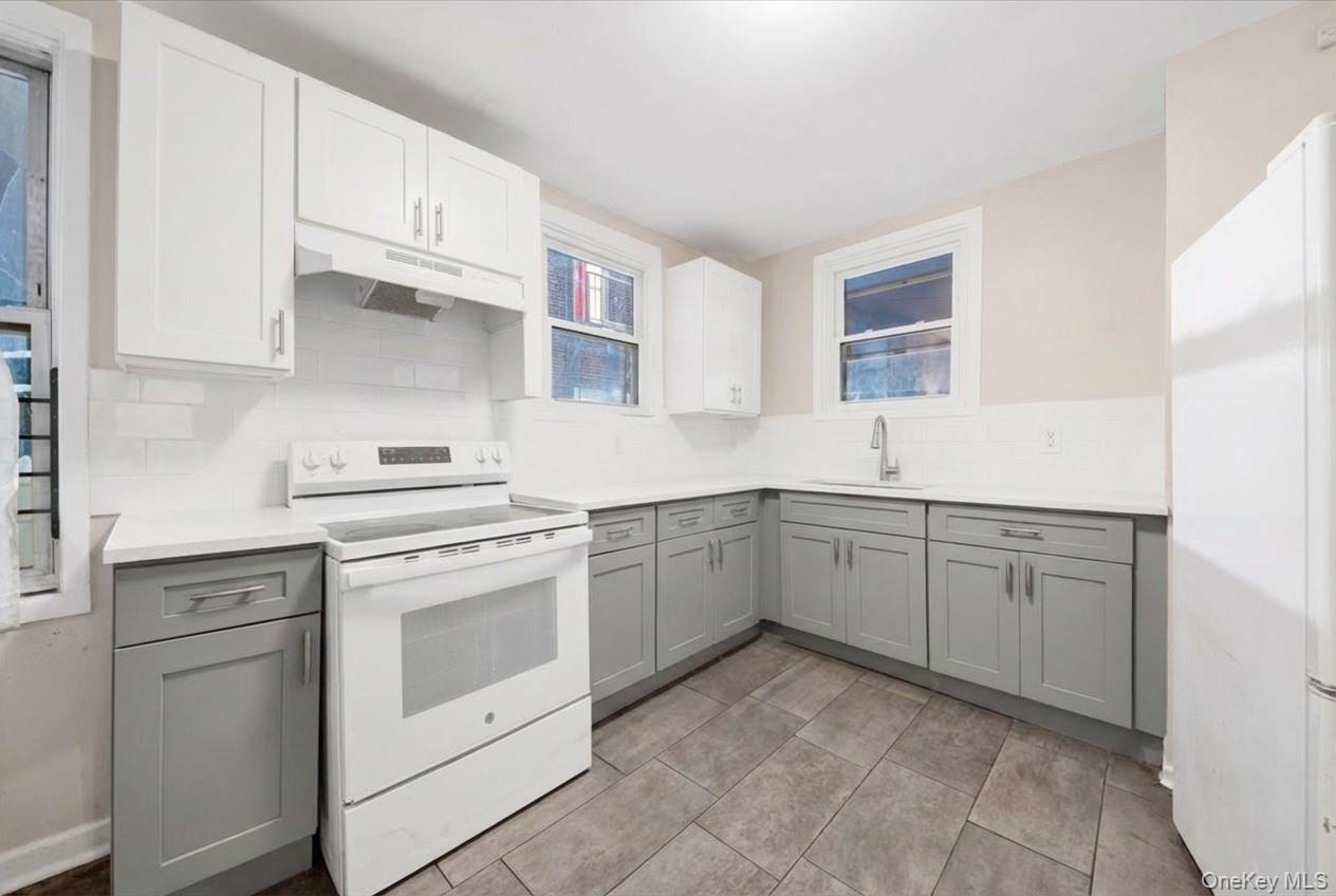 Eat-in Kitchen with gray cabinets, white appliances, under cabinet range hood, white cabinets, and tasteful backsplash