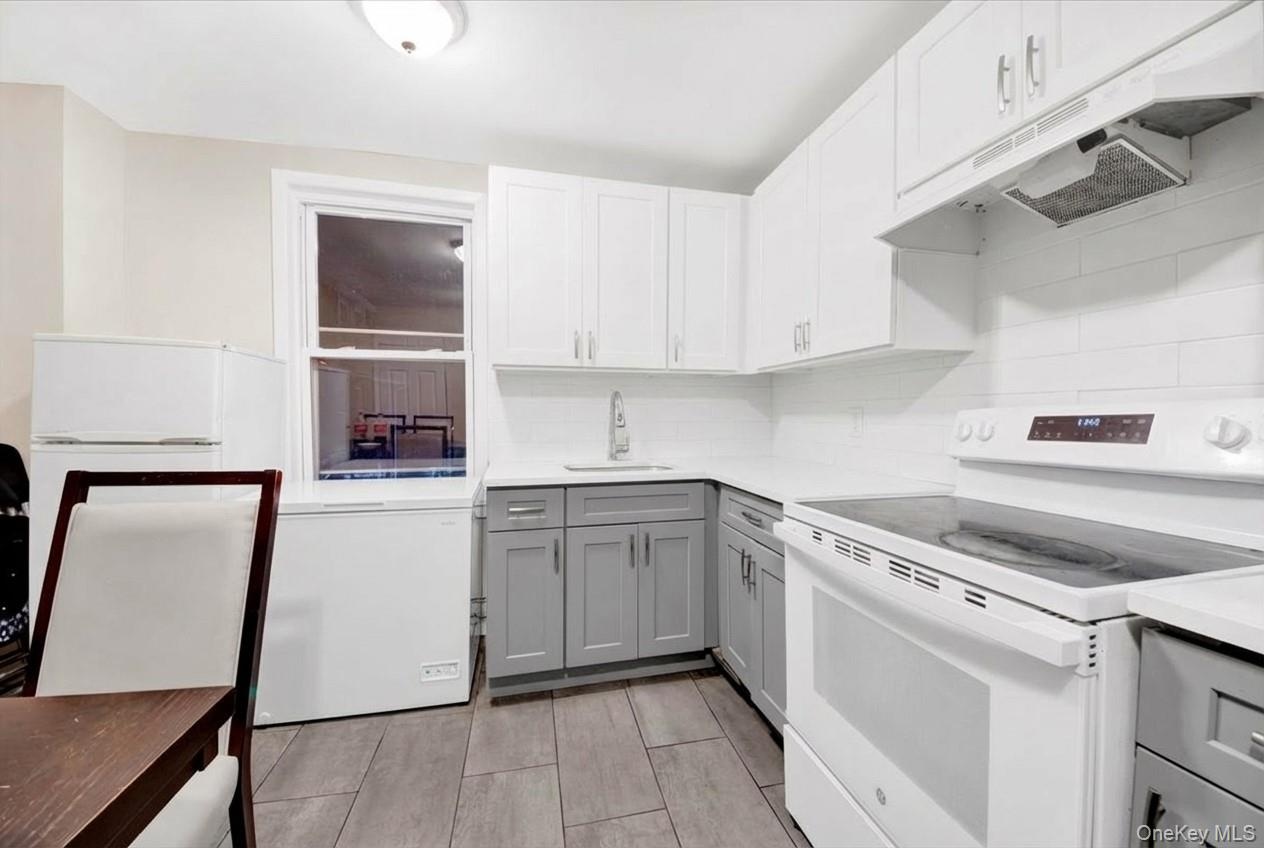 Kitchen featuring white appliances, gray cabinets, under cabinet range hood, and white cabinets