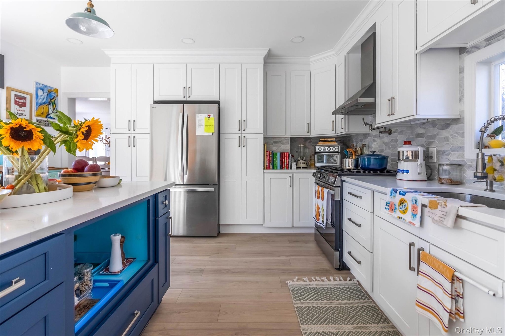Kitchen featuring blue cabinets, stainless steel appliances, white cabinetry, wall chimney range hood, and recessed lighting