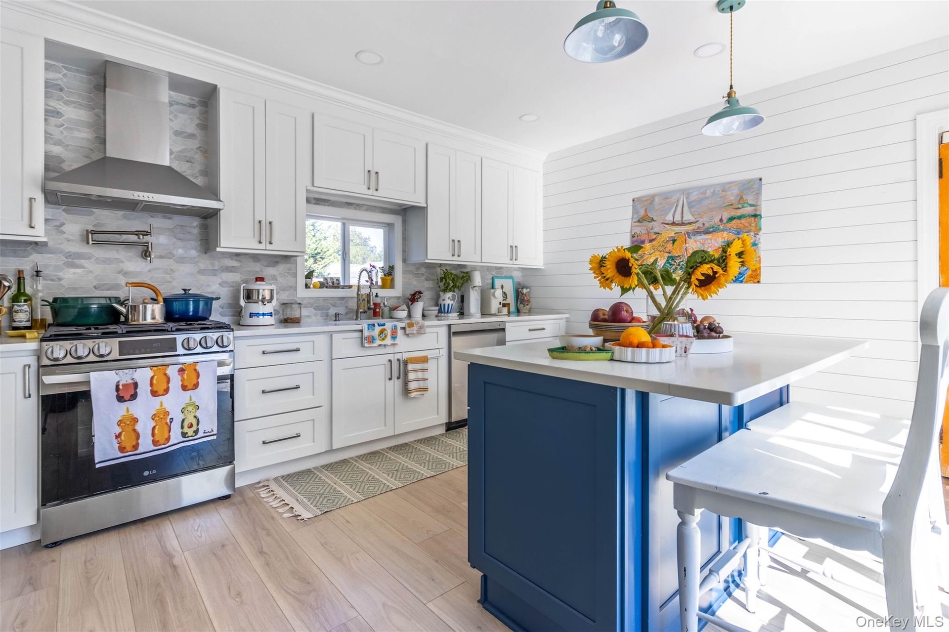 Kitchen featuring blue cabinetry, white cabinets, appliances with stainless steel finishes, wall chimney exhaust hood, and decorative light fixtures