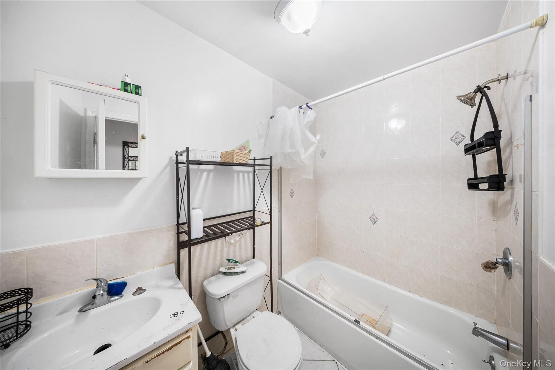 Full bath featuring shower / bath combo, vanity, tile walls, and wainscoting