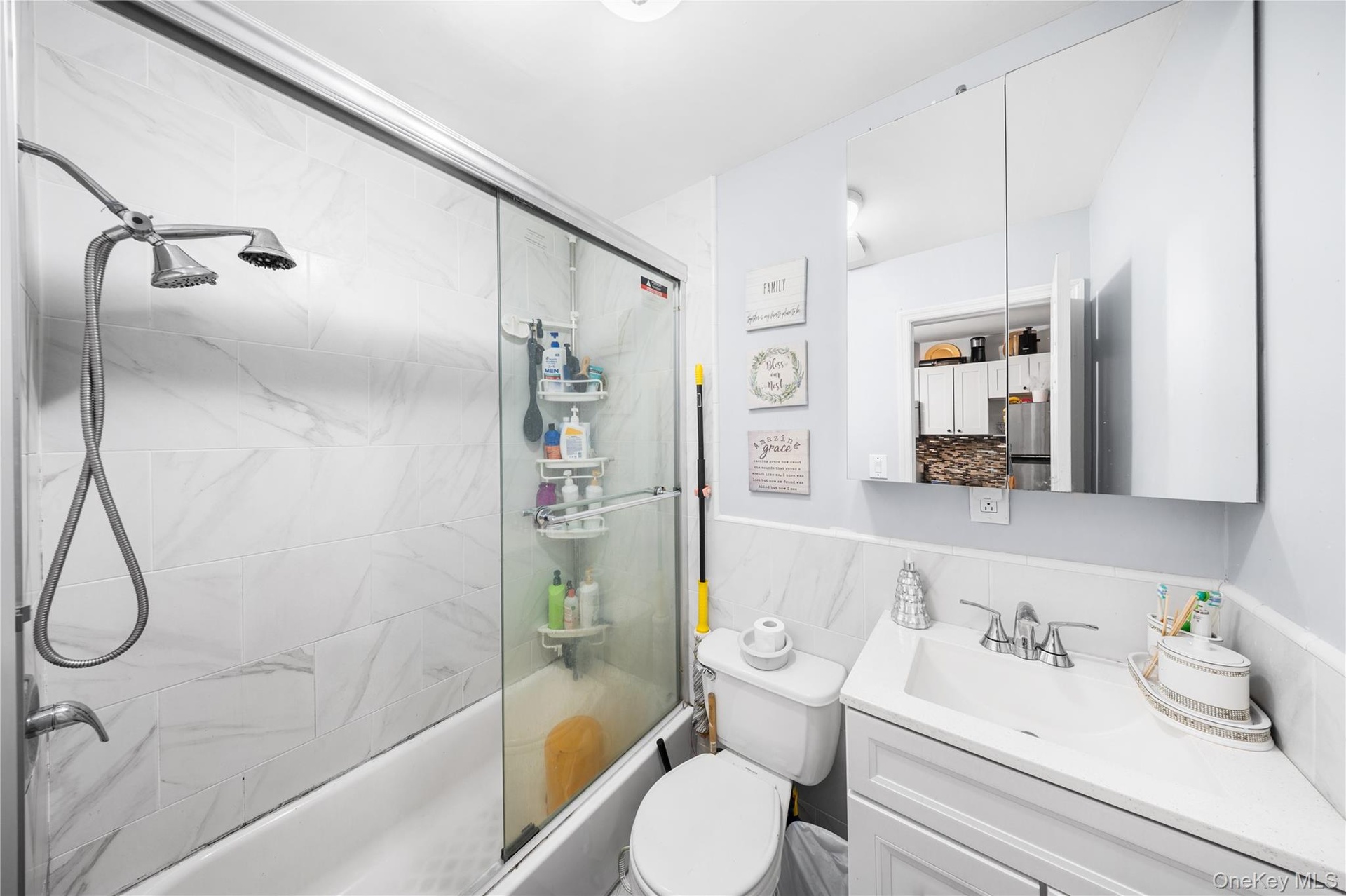 Bathroom with vanity, bath / shower combo with glass door, and a wainscoted wall