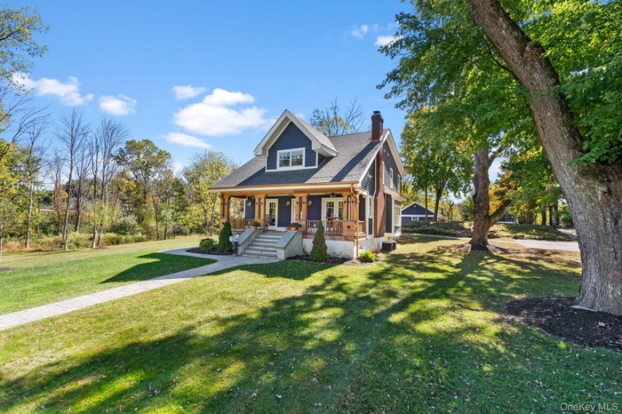 View of front of house featuring covered porch, a chimney, a front yard, and roof with shingles
