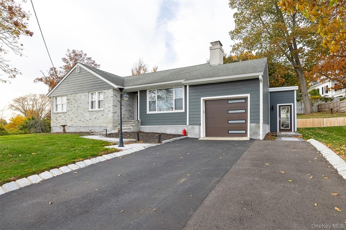 View of front of house featuring a front lawn, asphalt driveway, a chimney, a garage, and a shingled roof