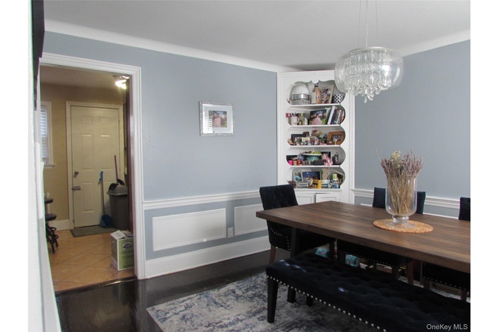 Dining area featuring dark wood-style flooring, a chandelier, a decorative wall, and wainscoting
