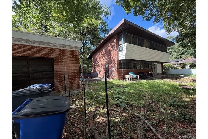 Rear view of house featuring a sunroom, brick siding, a garage, and a patio area