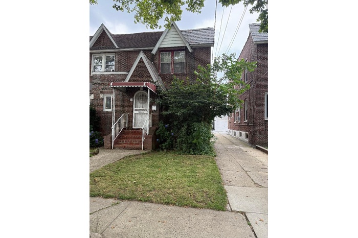Tudor-style house with brick siding, a front yard, a garage, and entry steps
