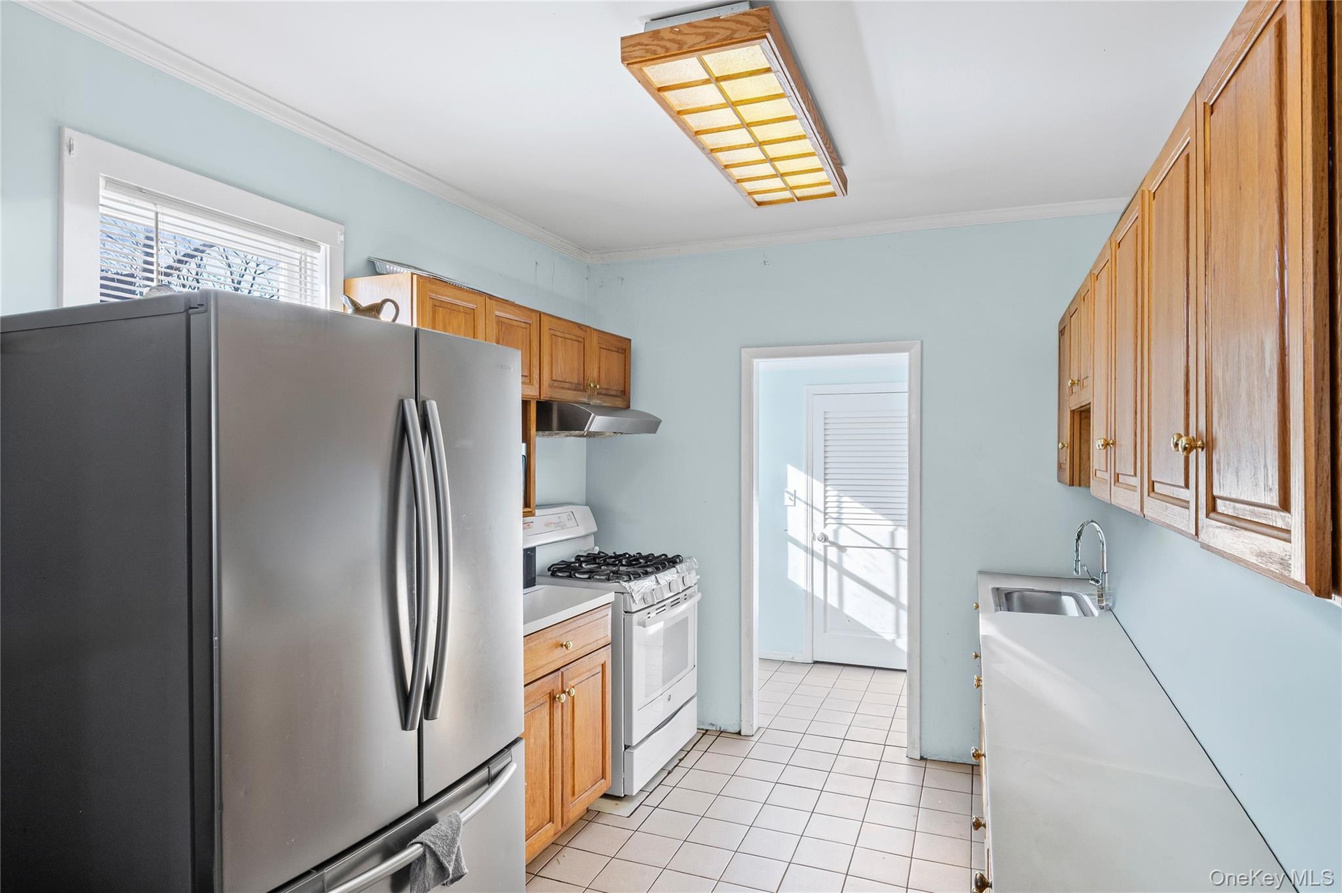 Kitchen featuring freestanding refrigerator, white range with gas stovetop, light countertops, crown molding, and light tile patterned flooring