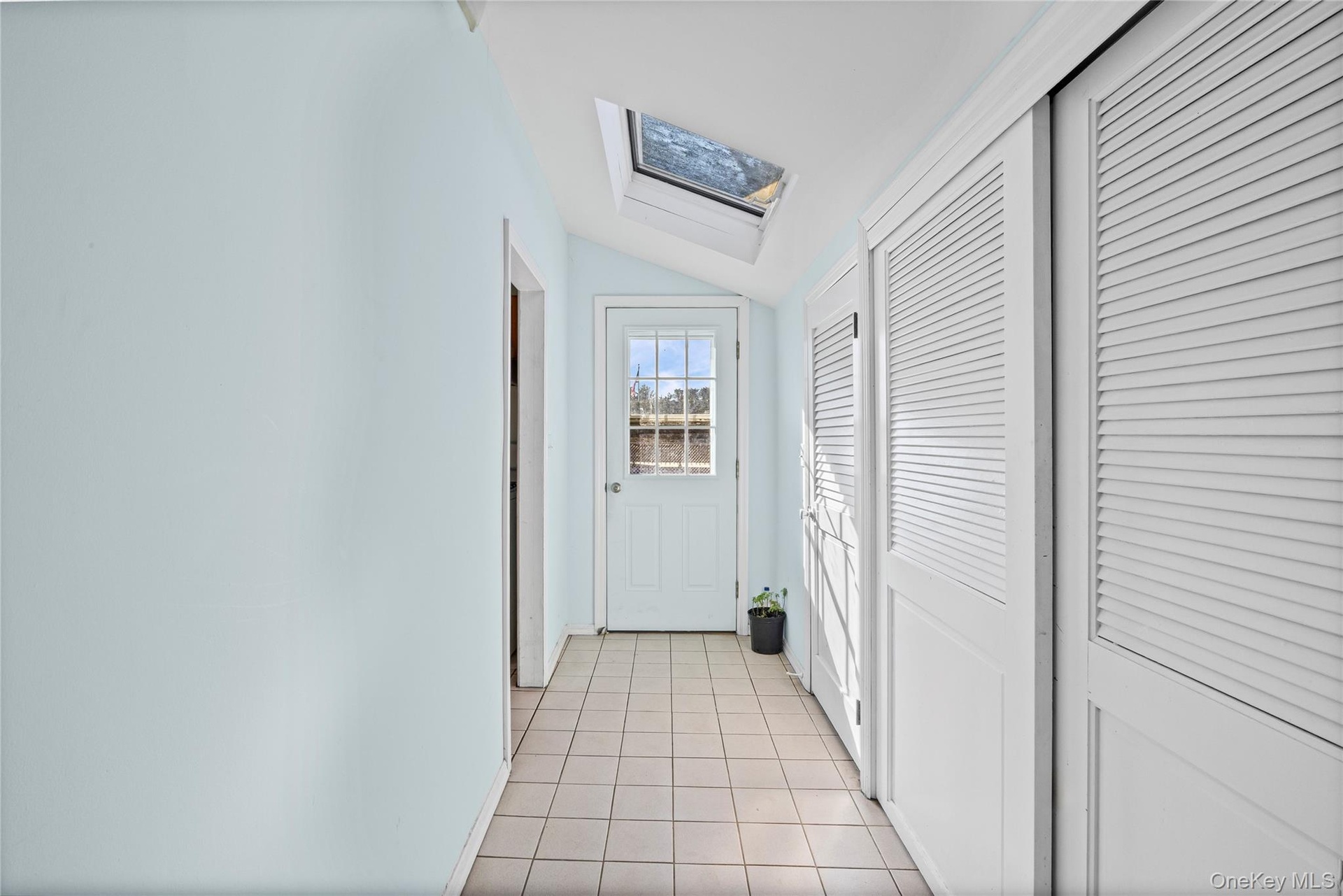Corridor of closets featuring a skylight, vaulted ceiling