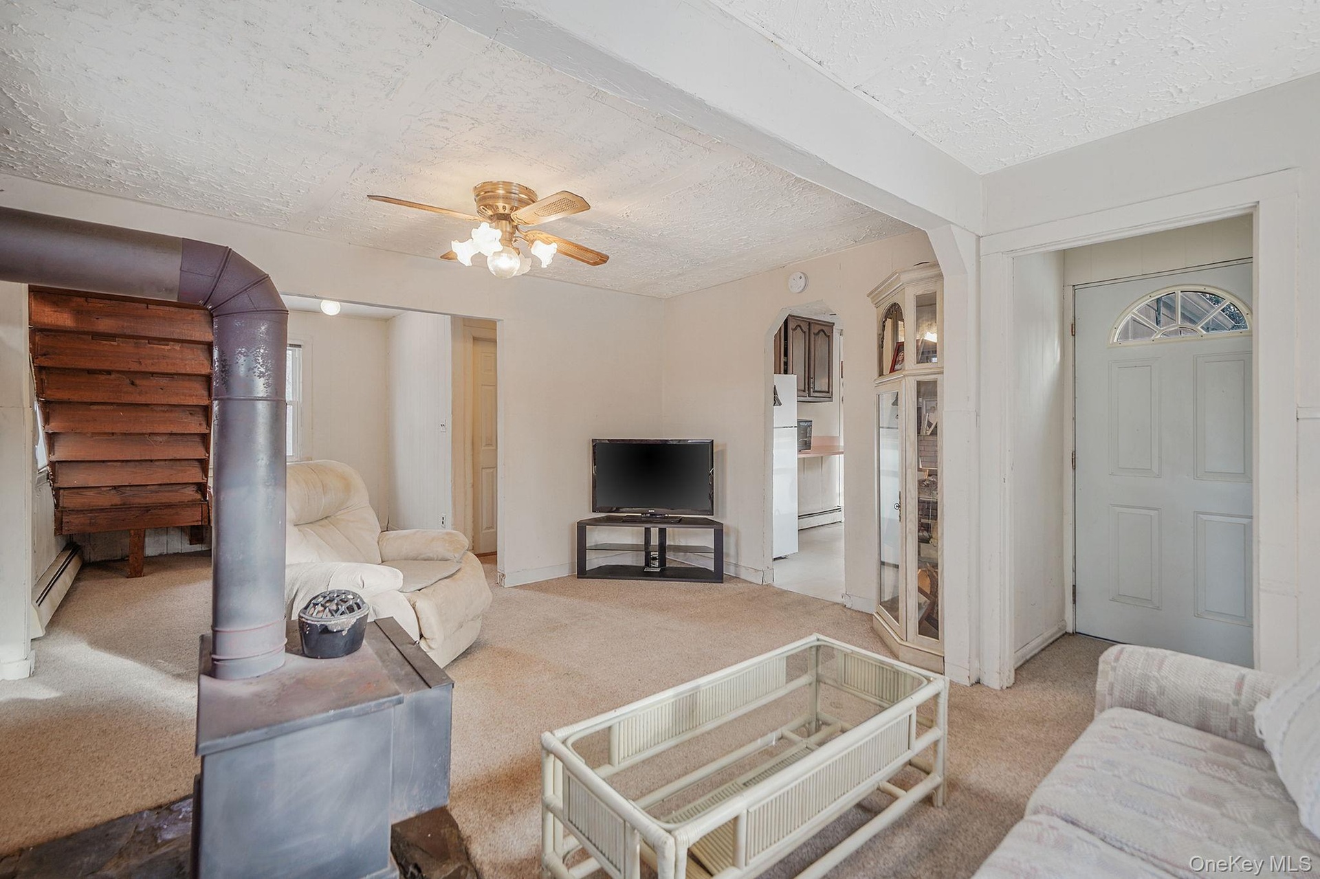 Carpeted living area with ceiling fan, arched walkways, a textured ceiling, and a baseboard heating unit