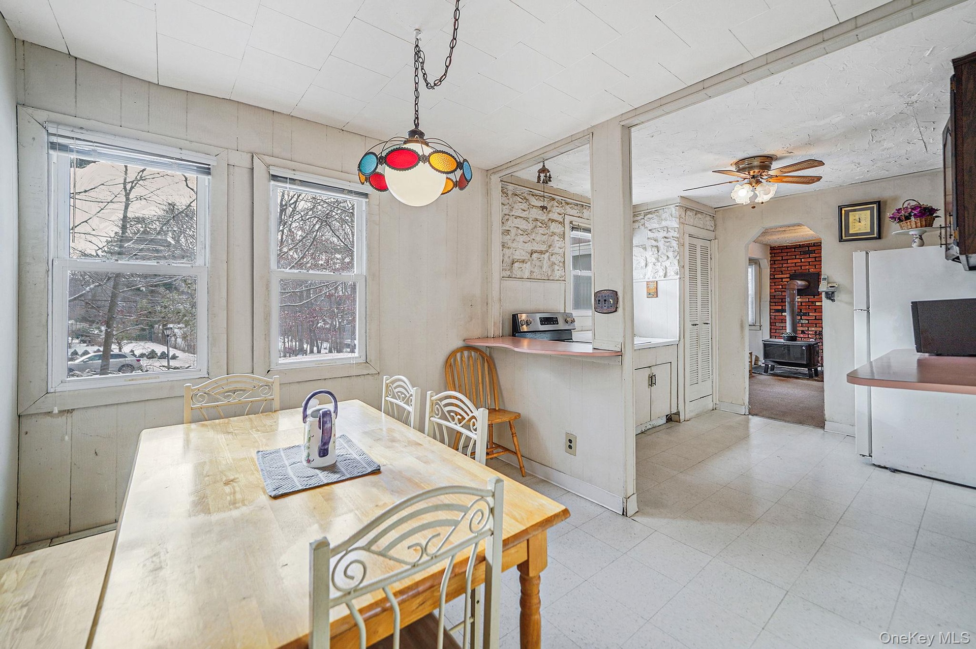 Dining space with a wood stove, ceiling fan, light flooring, and arched walkways
