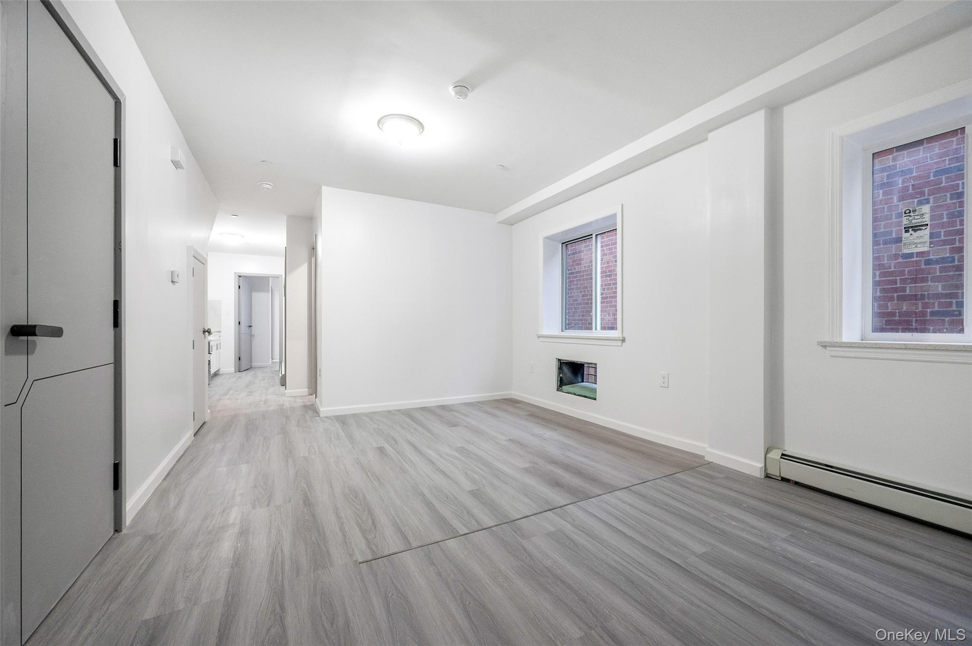 Unfurnished room featuring a baseboard heating unit, light wood finished floors, and a glass covered fireplace