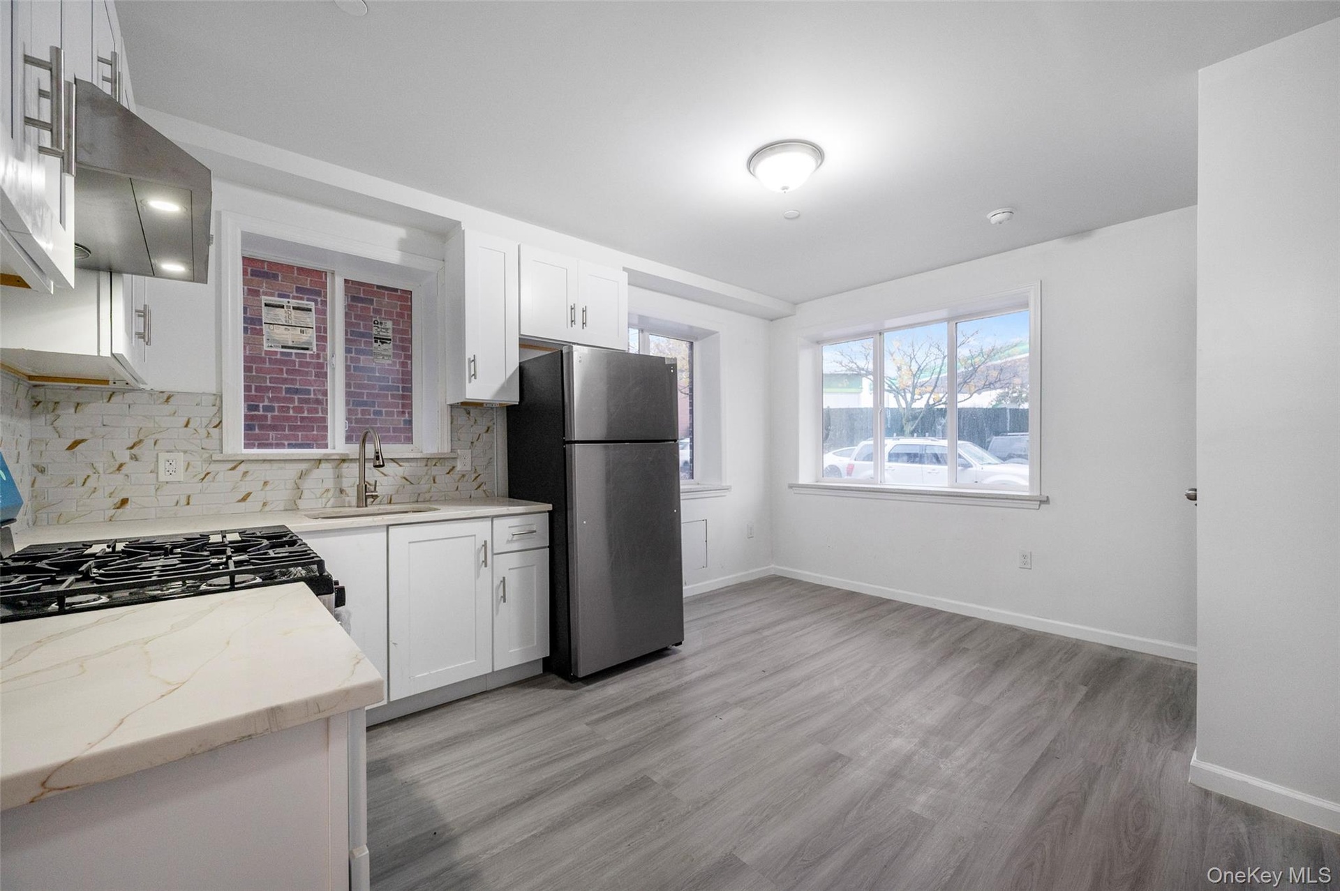Kitchen with light stone counters, freestanding refrigerator, white cabinets, range hood, and decorative backsplash