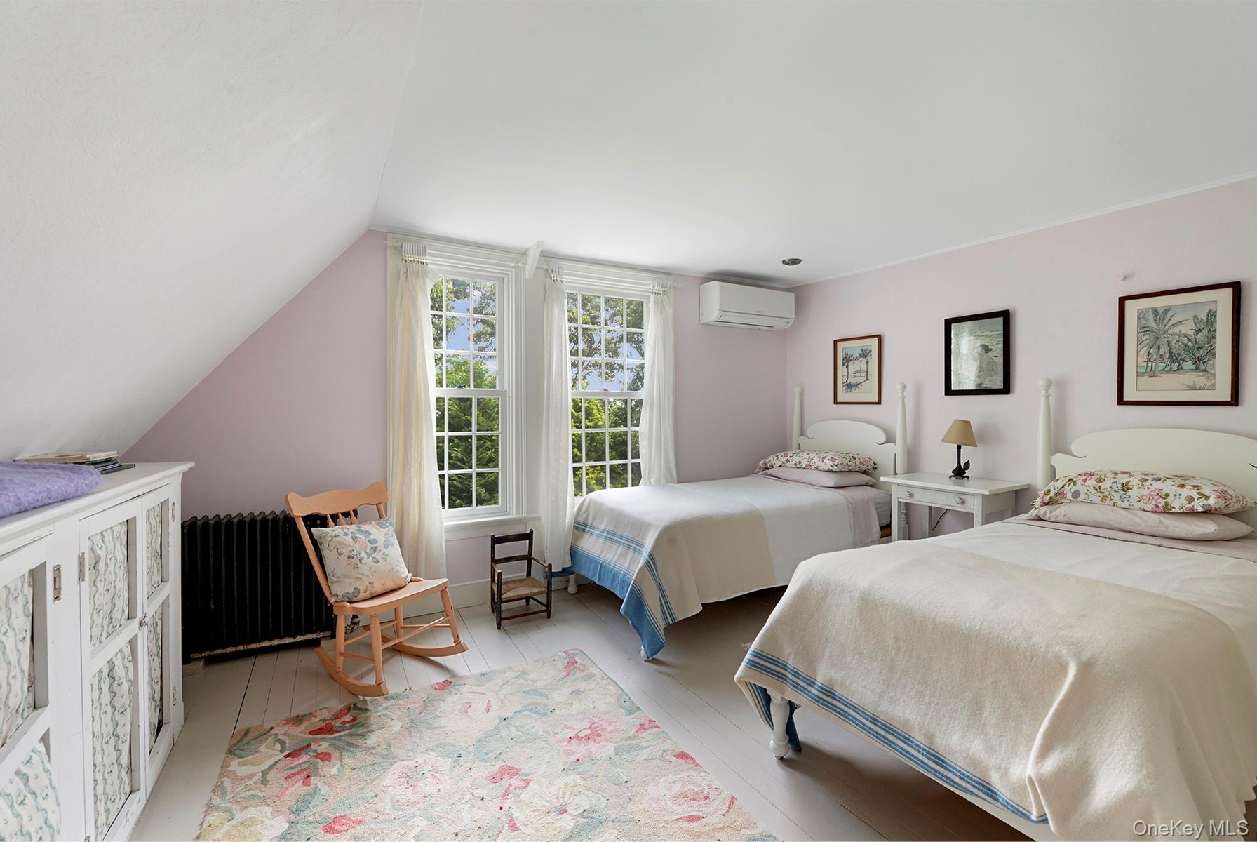 Bedroom with a wall mounted AC, radiator heating unit, vaulted ceiling, and light wood-style floors