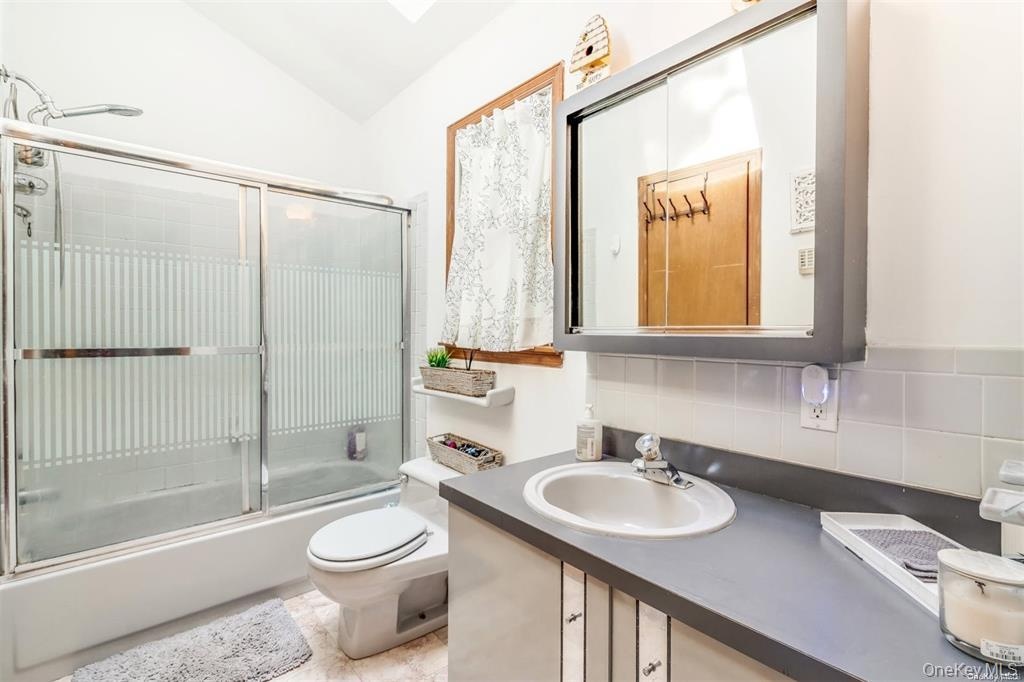 Bathroom with decorative backsplash, vanity, enclosed tub / shower combo, and vaulted ceiling