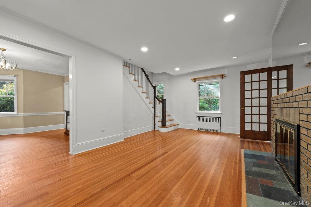 Unfurnished living room with light wood finished floors, recessed lighting, stairway, radiator, and a brick fireplace