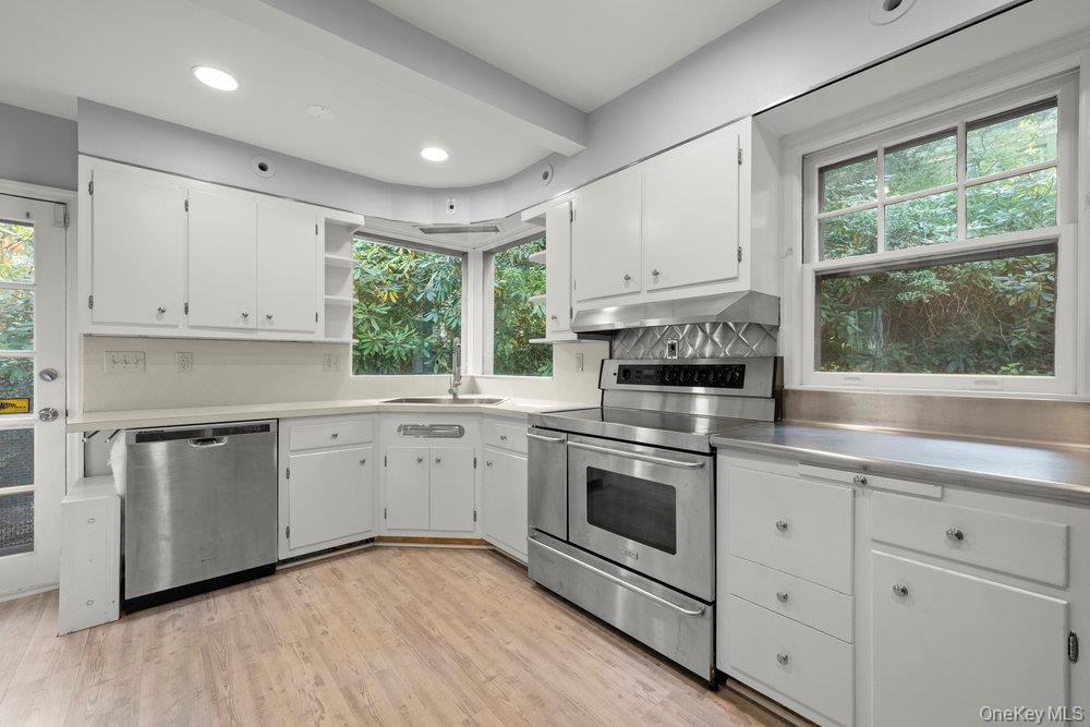 Kitchen featuring appliances with stainless steel finishes, white cabinetry, stainless steel countertops, open shelves, and light wood-style floors