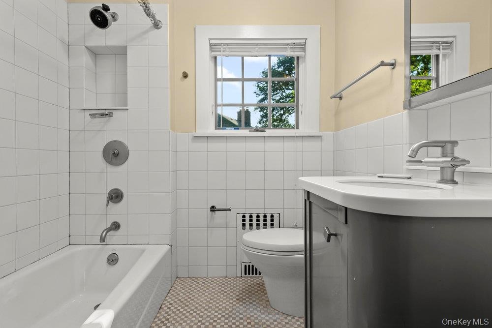 Full bathroom with tile walls, radiator heating unit, vanity, washtub / shower combination, and tile patterned flooring