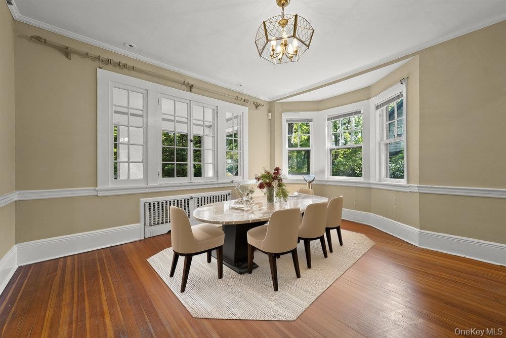 Dining space with hardwood / wood-style flooring, plenty of natural light, crown molding, radiator heating unit, and a chandelier