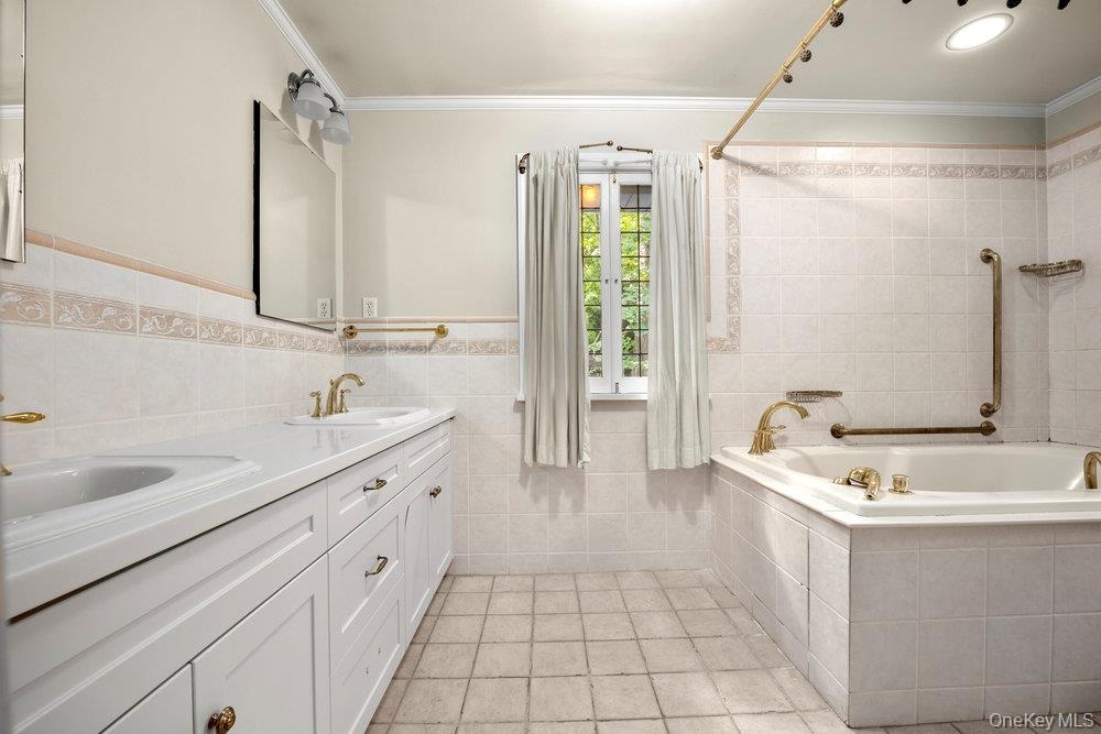 Full bath with tile walls, crown molding, double vanity, light tile patterned floors, and wainscoting