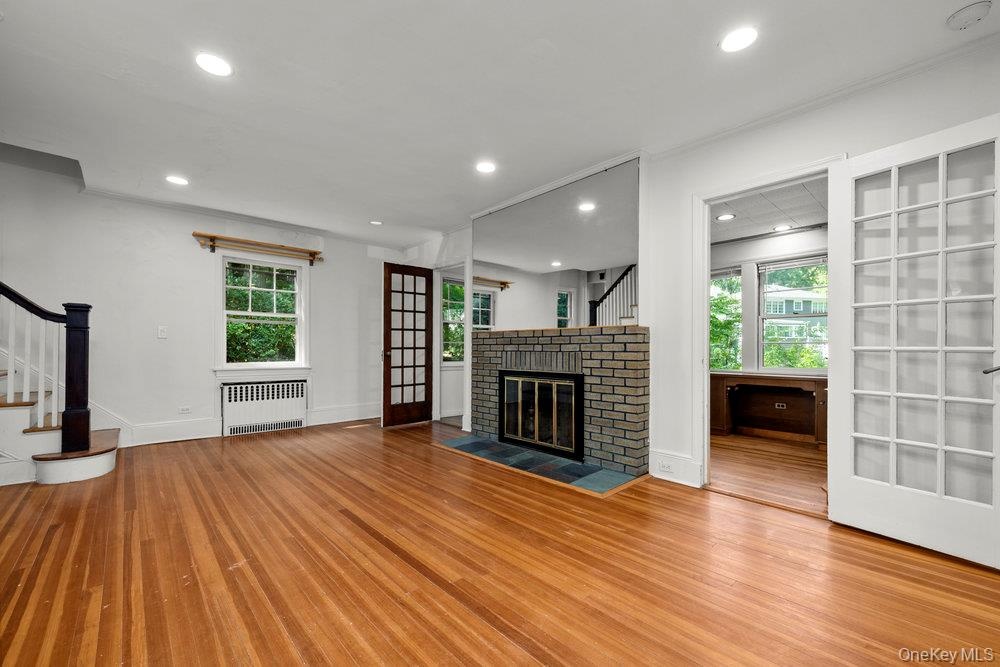 Unfurnished living room featuring stairs, recessed lighting, wood finished floors, radiator, and a brick fireplace