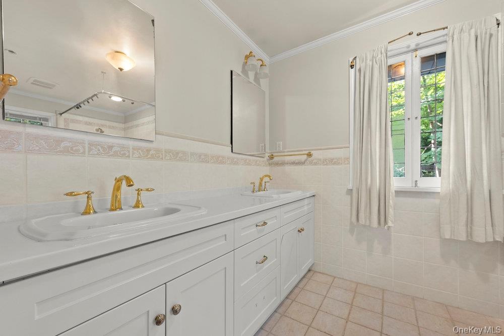 Full bath with light tile patterned floors, tile walls, ornamental molding, and double vanity