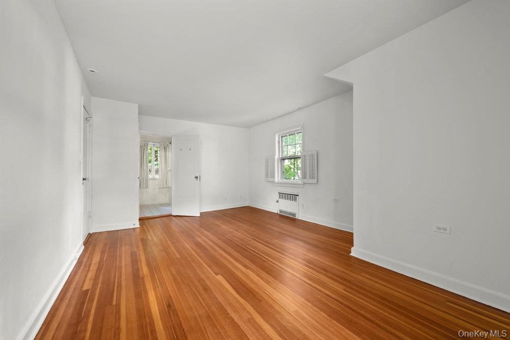 Empty room featuring wood finished floors and radiator heating unit