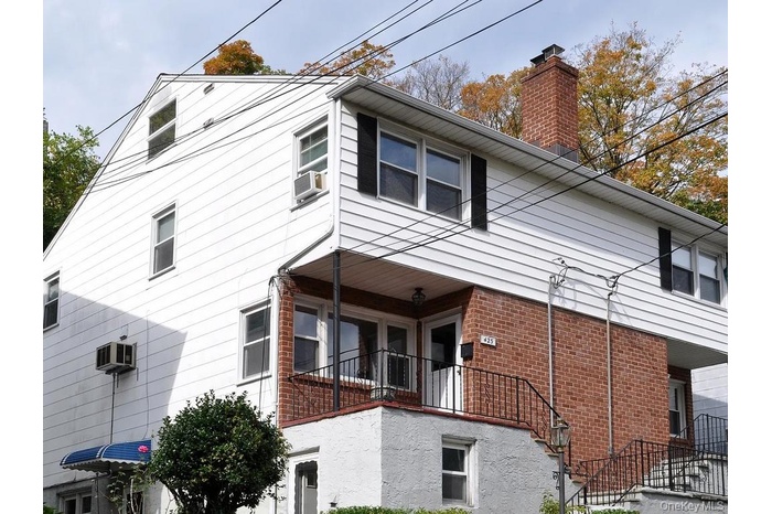 View of side of home with brick siding, a chimney, and a balcony