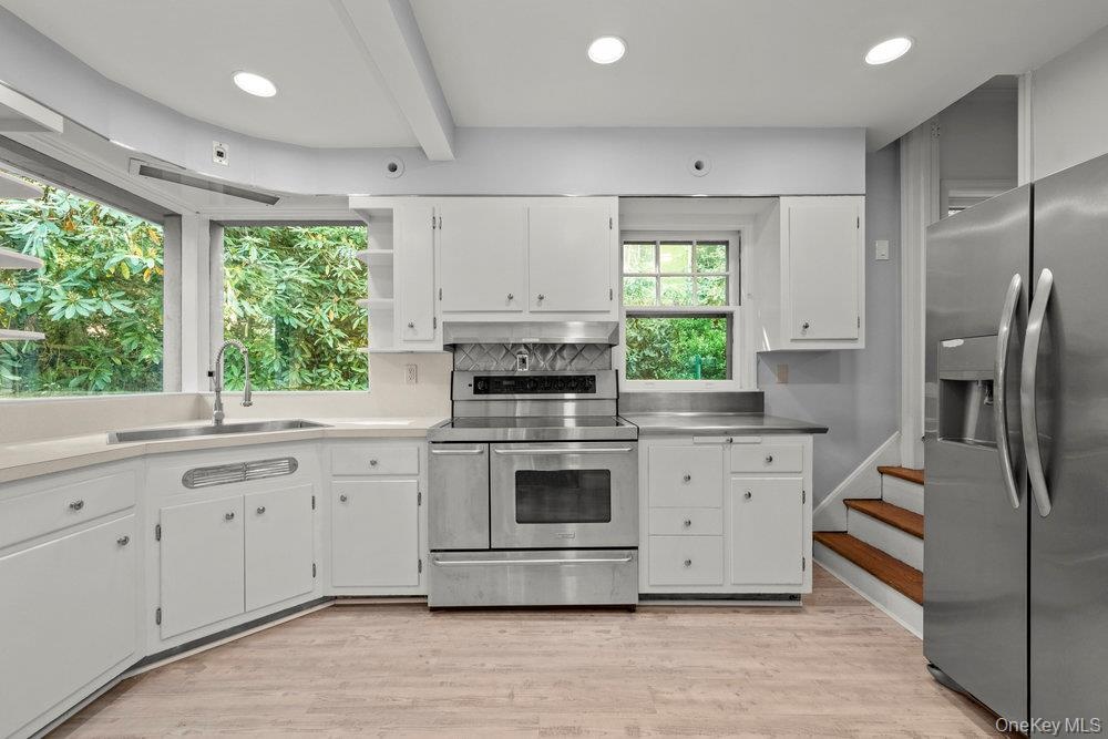 Kitchen with stainless steel appliances, stainless steel countertops, white cabinets, light wood-type flooring, and recessed lighting