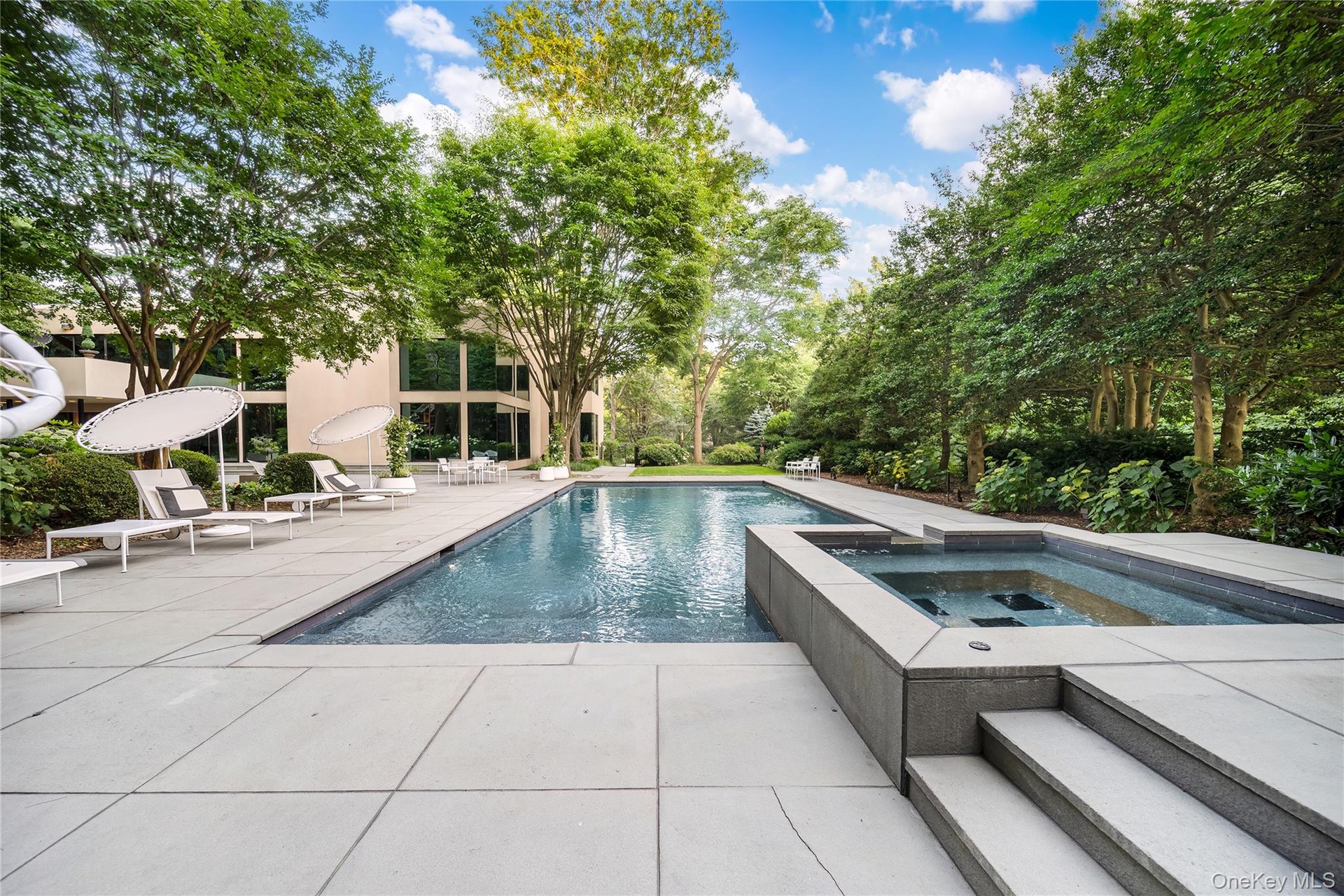 View of pool featuring a patio area, view of scattered trees, and a pool with connected hot tub