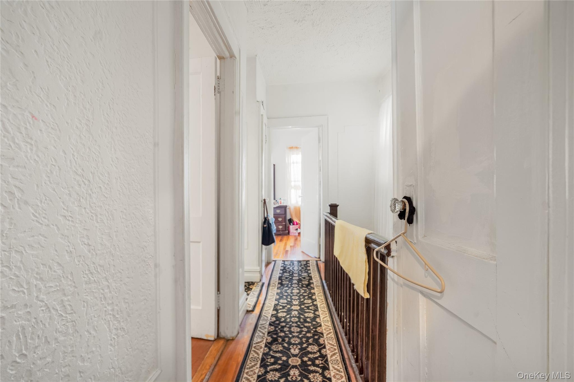 Hallway featuring dark wood-style floors, a textured ceiling, an upstairs landing, and a textured wall