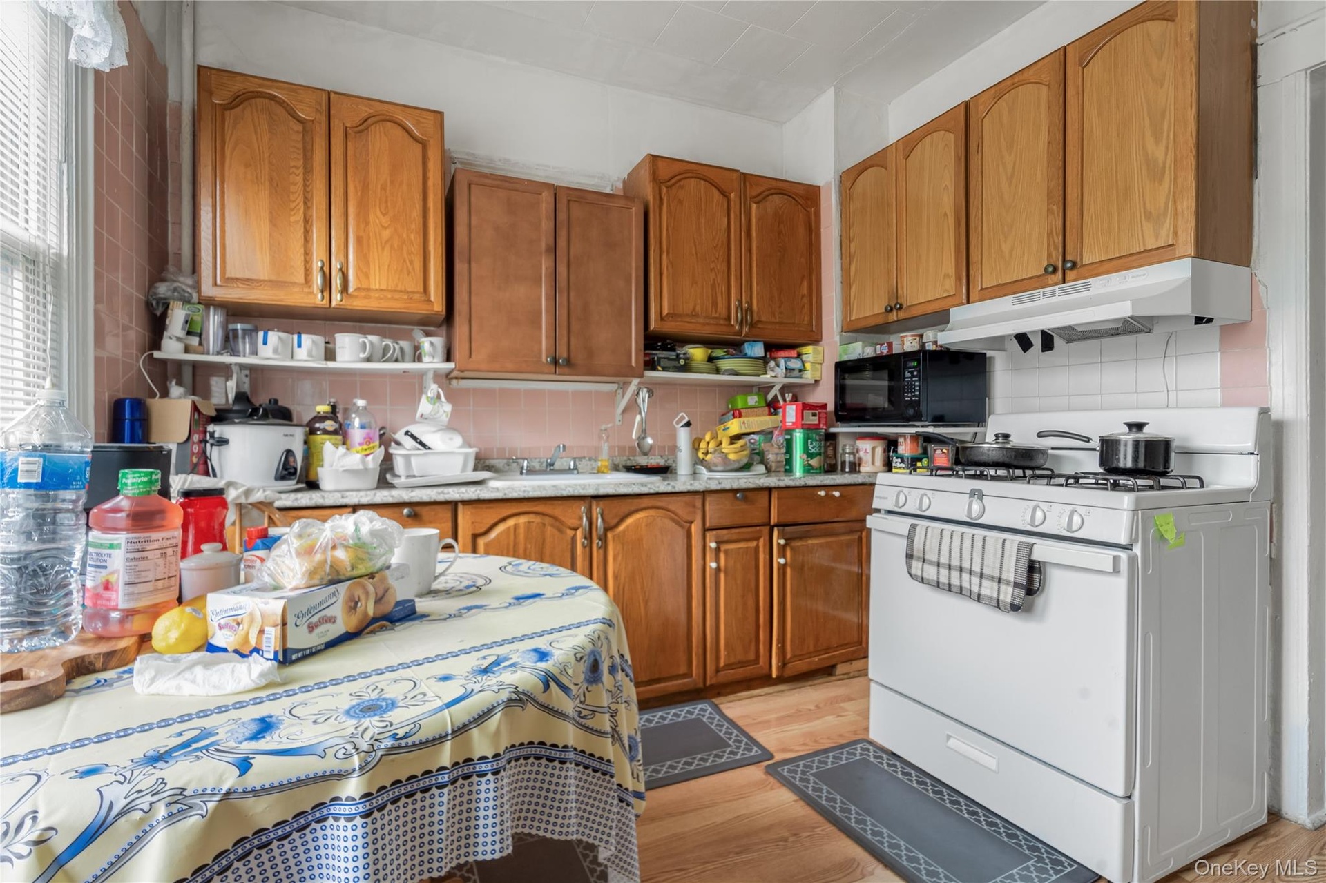Kitchen featuring white range with gas stovetop, brown cabinets, light wood-style floors, black microwave, and backsplash