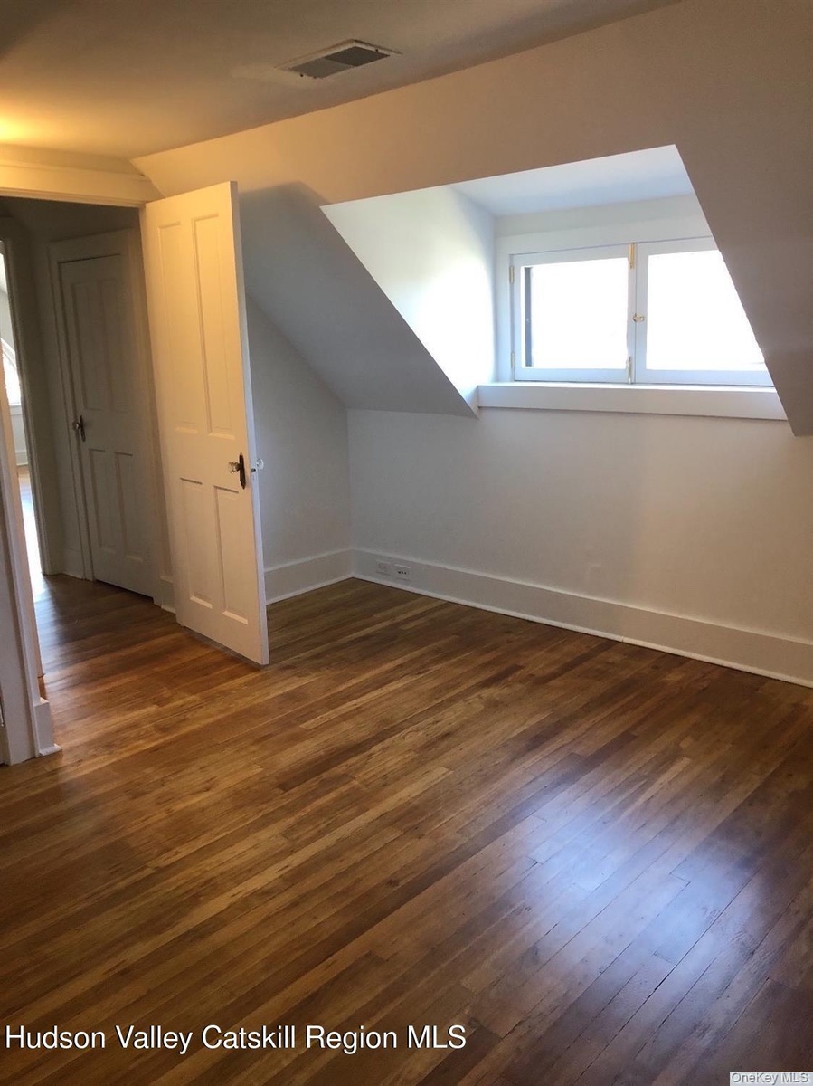 Additional living space with dark wood-style floors and vaulted ceiling