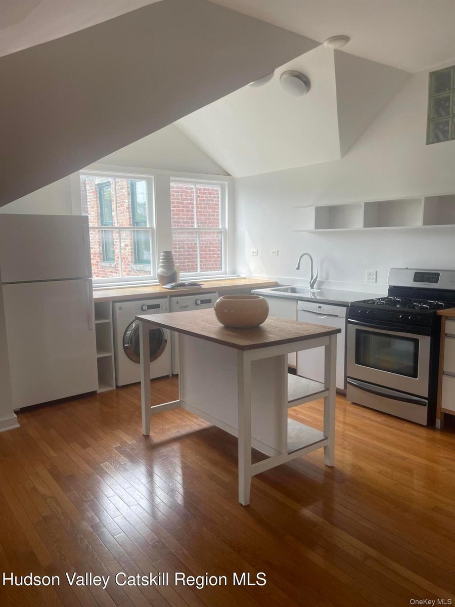 Kitchen featuring white appliances, washer / dryer, open shelves, lofted ceiling, and light wood-type flooring
