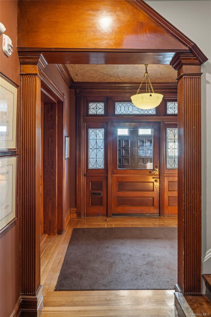 Foyer with light wood finished floors, crown molding, and decorative columns