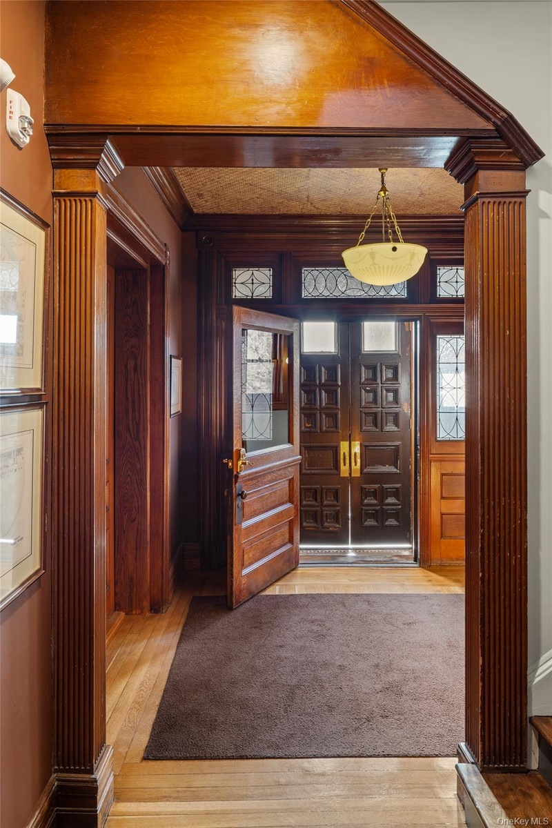 Foyer with light wood-type flooring, french doors, ornamental molding, and decorative columns