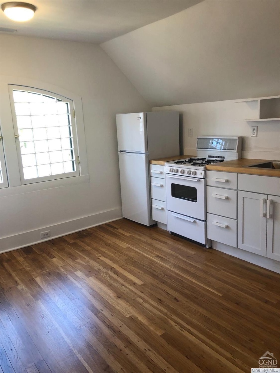 Kitchen featuring white appliances, lofted ceiling, white cabinetry, dark wood-style flooring, and open shelves