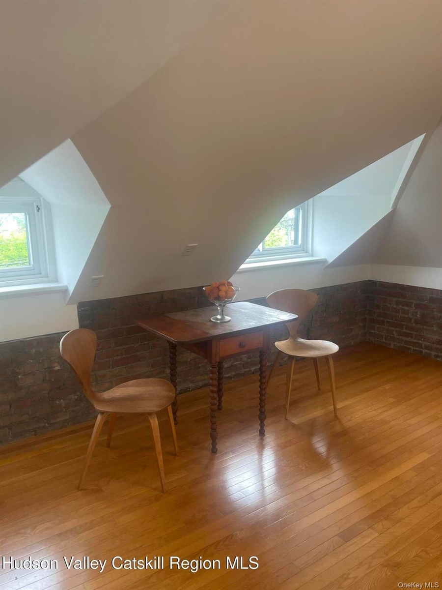 Bonus room featuring brick wall, lofted ceiling, light wood-style flooring, and healthy amount of natural light